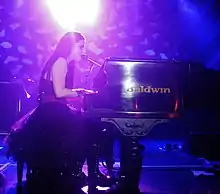 Young woman with long, dark hair singing and playing piano onstage