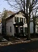 Photograph of the Fitzgeralds' Buffalo residence. The photo is taken during winter, and there are patches of snow on the ground. The two-story house is painted white with black trim. Its front features an Italianate portico with a triangular pediment crowning a segmental arch.