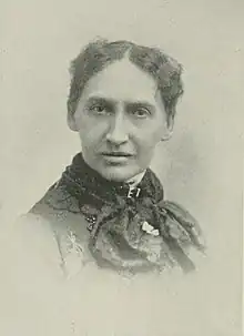 B&W portrait photo of a middle-aged woman with her hair in an up-do, wearing a dark, high-collared blouse.