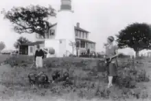 Photo of keeper Fannie Salter and her son, Charles, with turkeys raised at the Turkey Point Light Station. The lighthouse and keeper's homestead are visible in the background.