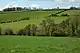 Hilly grazing farmland with trees and hedgerows with Cae Camp in the distance on the skyline