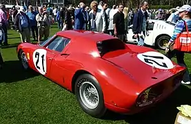 Back view of a red Ferrari sports car standing on a grass field at a car show