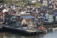 A short stone pier with a lifeboat on the right and many buildings behind