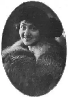 A smiling young woman, wrapped in a fur, wearing a dark hat. The black-and-white photo is in an oval frame.