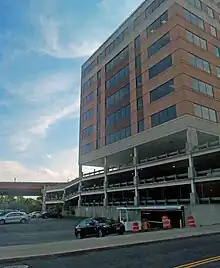 An empty parking lot next to a tall modern brick building above a parking garage