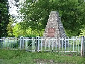 Stone cairn with plaque affixed behind a steel picket fence