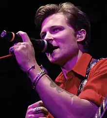 A young man wearing a red shirt, singing into a microphone