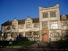 Part of a stone building seen from the front.  Towards the right of the picture is a three-storey square tower containing a door.  The building extends on both sides of the tower and has two storeys;  the portion of the building to the left contains two gables.