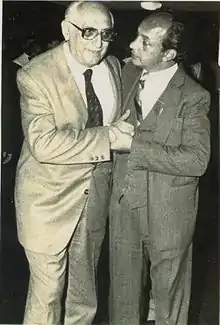 Two men in suits, standing and talking