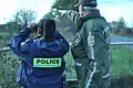 An SQ agent with a pre-2016 uniform observing the border with an RCMP agent