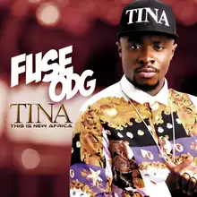 Fuse ODG is pictured wearing a colourful shirt and a black cap with the letters "TINA" on it, in front of a mostly dark-red background of blurred lights.