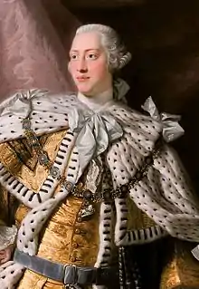 Three-quarter-length portrait in oils of a clean-shaven young man in eighteenth century dress: gold jacket and breeches, ermine cloak, powdered wig.