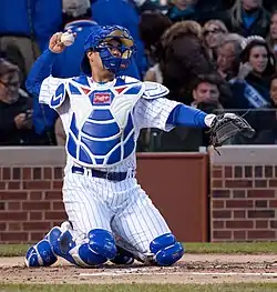 A baseball player in a white uniform and blue catcher's gear