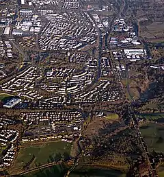 Greenfaulds from the air photographed from above Condorrat. The rugby club is at the bottom with Greenfaulds High School on the right. The view is up the railway line with the Town Centre in the background. Carbrain is above Greenfaulds with Lenziemill to the right.