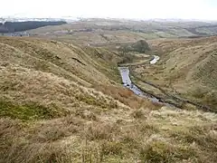 A small stream meandering through a narrow valley with snow-covered hills in the distance