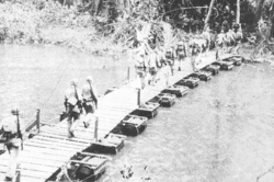 A U.S. Marine patrol crosses a pontoon bridge built by US Navy Seabees on the Lunga River in 1942