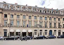 Color photograph of a building, seen slightly in profile, in the classical four-storey style. The facade features chains of refractions on the ground and mezzanine floors, as well as alternating dormers and oculi.