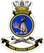 A ship's badge. A naval crown sits on top of a black scroll with "MELBOURNE" written in gold. This is atop a yellow, rope-patterned ring, in which the head and torso of a kangaroo, holding a crown, is depicted. Below the ring are a stone axe and a nulla nulla sitting on top of a boomerang. At the bottom of the badge is a black scroll with "VIRES ACQUIRIT EUNDO" written.