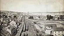 Cityscape bisected by central traintracks, with dense buildings to the left and harbourfront to the right