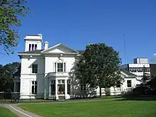 A rendered Italianate-style building with a bay window and a belvedere