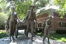 Outdoor statue of a man pulling a handcart, with family members on foot around the cart