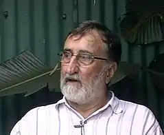 An elderly but fit-looking white man with a beard, in mid-sentence