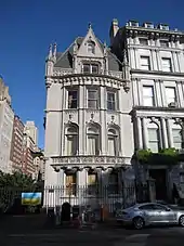 The facade of the Sinclair House as seen from across Fifth Avenue. The facade contains a curved, projecting pavilion as well as horizontal belt courses between each story. On the right is the flat limestone facade of the neighboring house at 973 Fifth Avenue.