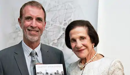 A head-and-shoulders portrait of a man in a suit standing alongside an elegantly dressed woman