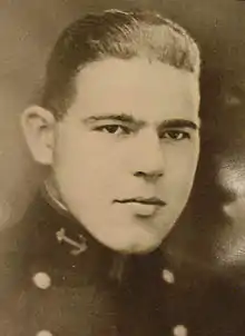 Head of a young white man with hair combed back at the top and short on the sides, wearing a dark jacket with two columns of buttons down the chest and an anchor emblem on the upright collar.