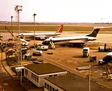 A South African Airways Boeing 707 in former orange, blue and white livery in the background at London Heathrow Airport, parked next to a BOAC Vickers VC10.