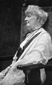 An older white woman with white hair, seated, photographed in profile; she is wearing a white lacy shawl