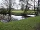 Square grassed area surrounded by moat and some trees with a wooden bridge