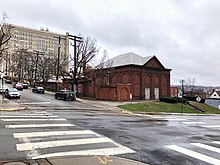 A photo of the Herron Hill Pumping Station in 2019. It is a red brick building with bricked-up windows and a white roof.