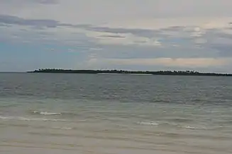 Small low green island in blue sea, at about two km.  One beach can be made out.