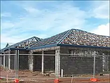 A hip roof construction in Northern Australia showing multinail truss construction. The blue pieces are roll formed metal roof battens or purlins. This roof is built with purpose-made steel hook bracket which is bolted to the truss with M16 bolt. The bracket is bolted to an M16 bolt cast in situ, embedded 300 mm (12 in) into the reinforced concrete block wall.  This system is typically in place every 900 mm (35 in) around perimeter