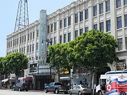 A street view of a wide, white building. In the center is a large vertical sign that says "Pacific".