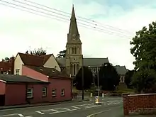 A church seen beyond houses and trees with a prominent tower and spire