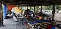 The inside of a wooden picnic shelter in a park with a roof and no walls with people in sleeping bags, couches and various other signs of occupation