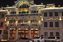 A photo of the Hongji Grand stage. The building is regal in appearance and well lit amid the dark sky. The structure has golden highlights amid a white concrete facade.