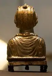 The golden back of a statue of a lady made from metal standing on dumpy feet