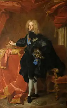 Standing man with light, curly hair, dressed in dark-colored royal finery