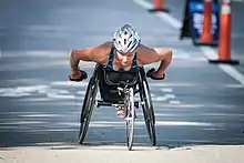 Women in blue and black clothes and a silver helmet racing in a black wheelchair.