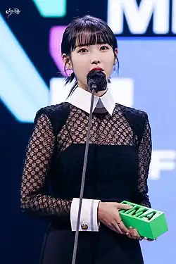 IU holding a MMA trophy while talking into a microphone