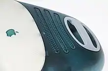 Detail of the back of a curved, blue-green translucent computer; a white plastic handle and ventilation hole are visible.