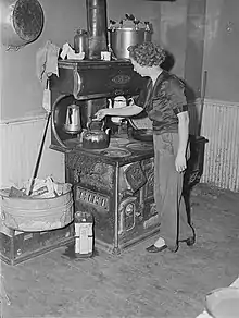 Metal can of motor oil next to wood burning stove and oven; used for getting the fire going; 1940