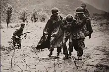 Capt. Emil Kapaun, right, a chaplain with the 3rd Battalion, 8th Cavalry Regiment, helps evacuate an exhausted soldier from the battlefield.