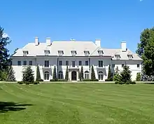 White mansion with four chimneys, trees lining the front, and many windows