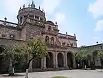 Entrance to a major stone building with colonnades and bells above the main entrance.