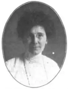 A photograph of a white woman in an oval frame; she is wearing eyeglasses and a white blouse with a high collar