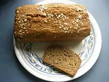 dark brown, rectangular loaf topped with flecks of white powder and slice sitting on plate